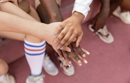 Das Bild zeigt, wie Kinder beim Sport ihre Hände in der Mitte aufeinanderlegen, um sich anzufeuern.