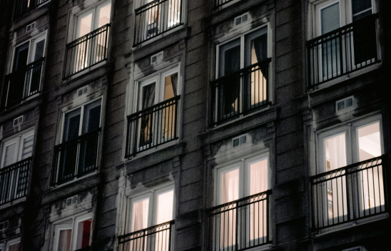 Häuserkomplex mit mehreren Etagen. Durch die Fenster ist zu sehen. dass in manchen Wohnungen Licht brennt, in anderen nicht. 