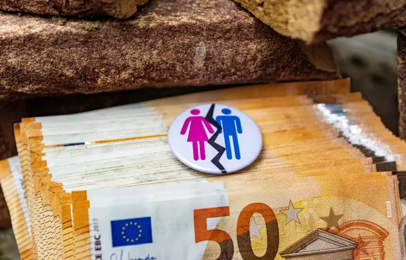 Mehrere 50€-Scheine, auf denen ein Button liegt. Auf dem Button abgebildet sind Piktogramme einer Frau und eines Mannes zu sehen, die durch einen Riss getrennt voneinander dargestellt sind