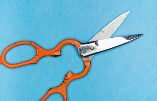 Eine geöffnete Schere mit orangefarbenen Griff liegt auf einer blauen Fläche. Eine geöffnete Schere mit orangefarbenen Griff liegt auf einer blauen Fläche.