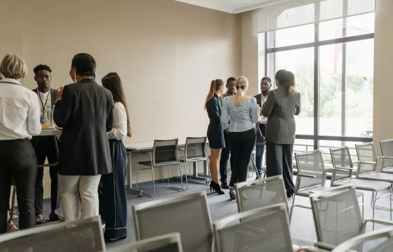 Zwei Gruppen von Personen stehen jeweils um einen Stehtisch herum und sprechen miteinander, im Vordergrund sind mehrere Stuhlreihen zu sehen Zwei Gruppen von Personen stehen jeweils um einen Stehtisch herum und sprechen miteinander, im Vordergrund sind mehrere Stuhlreihen zu sehen