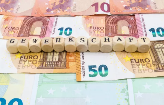 Auf verschiedenen Geldnoten sind Würfel mit Buchstaben aufgereiht. Die Würfel bilden das Wort "Gewerkschaft".