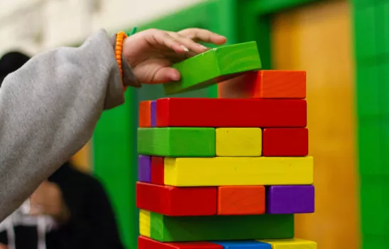 Buntes Jenga-Spiel, bei dem eine Kinderhand einen Stein nach oben legt. Buntes Jenga-Spiel, bei dem eine Kinderhand einen Stein nach oben legt.