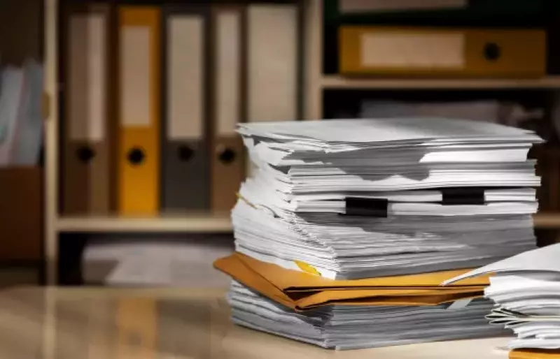 Ein Stapel Dokumente liegt auf einem Tisch vor einem Schrank mit Aktenordnern