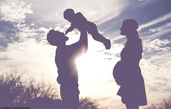 Die Silhouette einer Familie mit Kleinkind im Gegenlicht der Sonne auf einem Feld. 