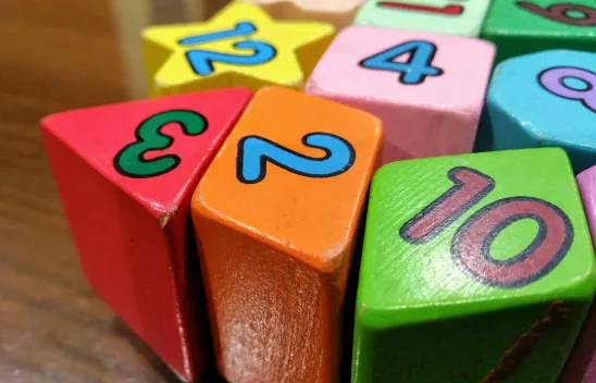 Bunte Spiel-Bauklötze in den Farben rot, orange, grün, rosa, hellblau und gelb. Darauf stehen jeweils Zahlen. 