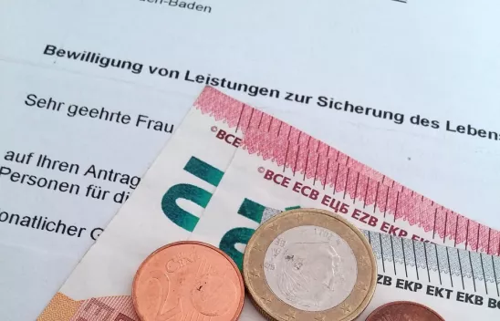 Ein Brief, auf dem "Bewilligung von Leistungen zur Sicherung des Lebens..." zu lesen ist, darauf liegen Münzen und Scheine
