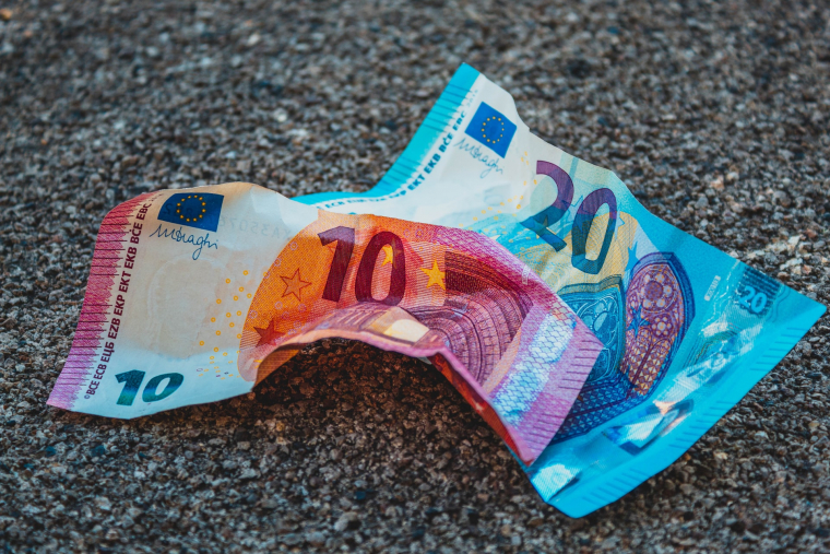 Ein Zehn-Euro-Schein und ein Zwanzig-Euro-Schein liegen zweknittert auf dem Asphalt. 
