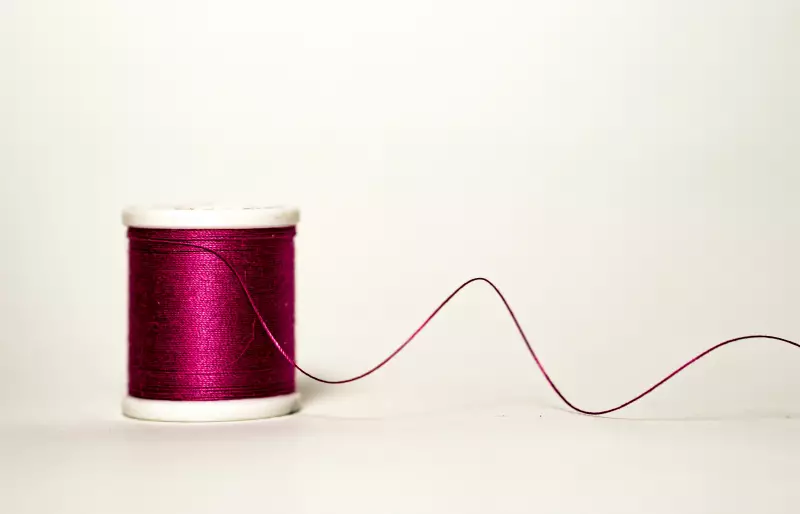 Eine Garnrolle, von der sich ein dunkelroter Faden abrollt.