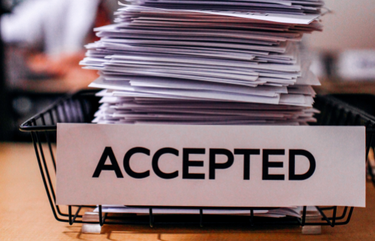 Ein Stapel Papier liegt in einem Korb, der mit dem Wort "ACCEPTED" beschriftet ist