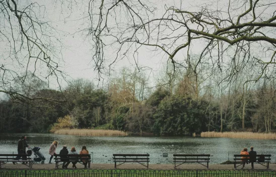 In einem Park sitzen Menschen unterschiedlichen Alters auf Bänken. Menschen mit Kinderwagen gehen vorbei. Alle sind aus der Ferne von hinten zu sehen. In einem Park sitzen Menschen unterschiedlichen Alters auf Bänken. Menschen mit Kinderwagen gehen vorbei. Alle sind aus der Ferne von hinten zu sehen.