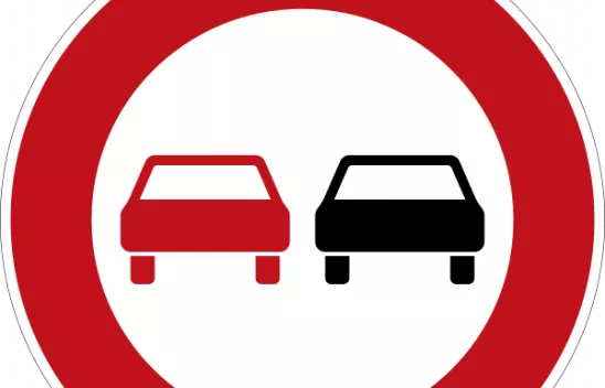 Ein Überholverbotsschild: Ein roter Kreis in dem links ein rotes Auto und rechts ein schwarzes Auto abgebildet sind. Ein Überholverbotsschild: Ein roter Kreis in dem links ein rotes Auto und rechts ein schwarzes Auto abgebildet sind.