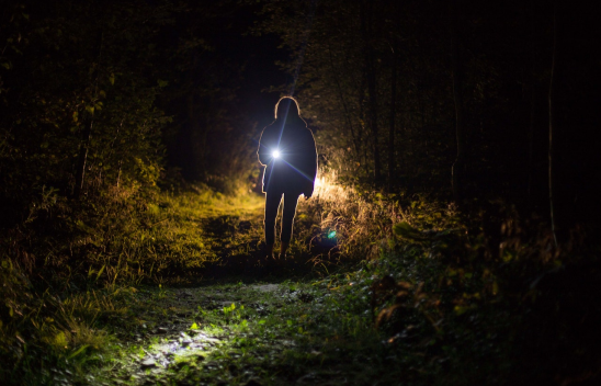 Eine Person steht im Dunkeln und leuchtet mit einer Taschenlampe Richtung Kamera.