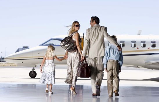 Eine Familie mit zwei Kindern ist schick gekleidet und läuft auf ein Privatflugzeug zu. 