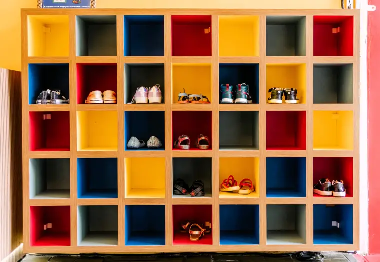 Ein buntes Schuhregal mit Fächern, in denen vereinzelt Kinderschuhe stehen.
