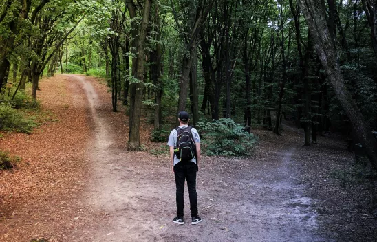 Jugendlicher steht an einer Weggabelung im Wald. Jugendlicher steht an einer Weggabelung im Wald.
