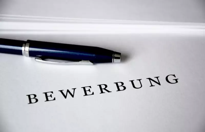 Schriftzug "Bewerbung" auf einem Blatt Papier, darüber liegt ein Kugelschreiber
