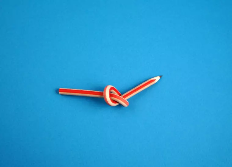 Ein verknoteter Bleistift auf blauem Hintergrund.