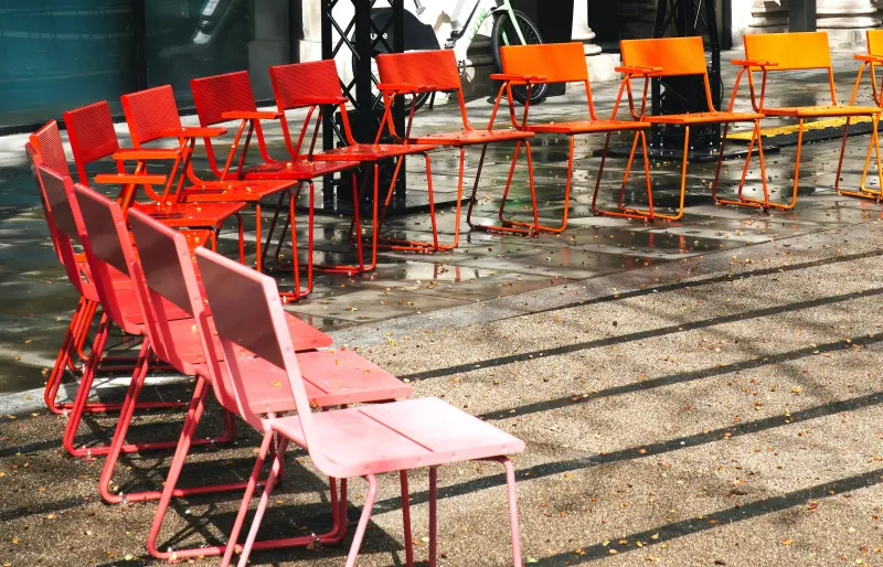 Stühle in den Farben gelb, orange und rot, stehen im Halbkreis auf einem öffentlichen Platz.