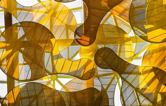 Mit transparentem, gelben Stoff bespannte organische Figuren vor einer Glaswand. Mit transparentem, gelben Stoff bespannte organische Figuren vor einer Glaswand.