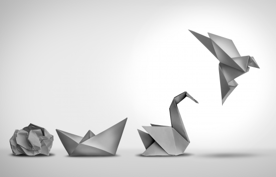 Eine Transformation von Papierfaltern bestehend aus einem Papierknäuel, einem Papierboot, einem Papierschwan und einem Papiervogel in Grautönen.