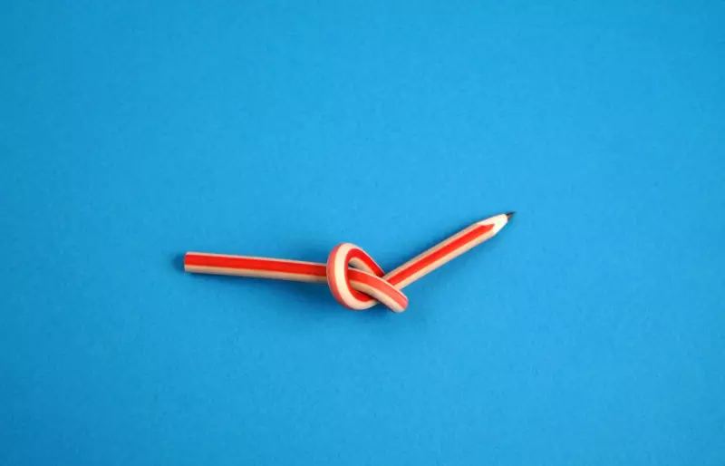 Ein verknoteter Bleistift auf blauem Hintergrund.