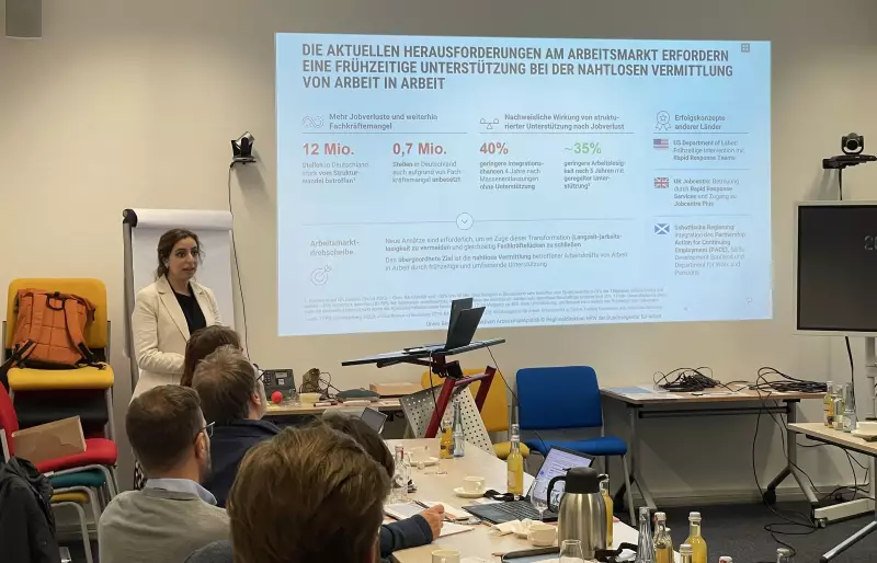 Eine Person steht vor einer Leinwand, auf der eine Präsentation läuft und hält einen Vortrag vor Publikum