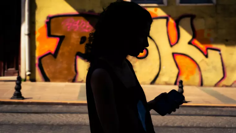 Die Silhouette einer Person, die auf ihr Smartphone schaut, vor einer Wand mit einem bunten Graffiti.
