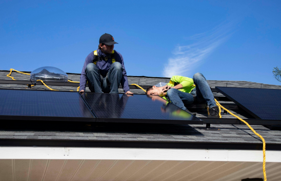 Zwie Personen arbeiten an einem Solarpanel auf dem Dach eines Hauses
