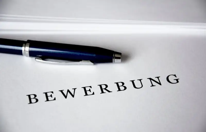 Ein Kugelschreiber liegt auf einem Blatt Papier, auf dem das Wort "Bewerbung" zu lesen ist