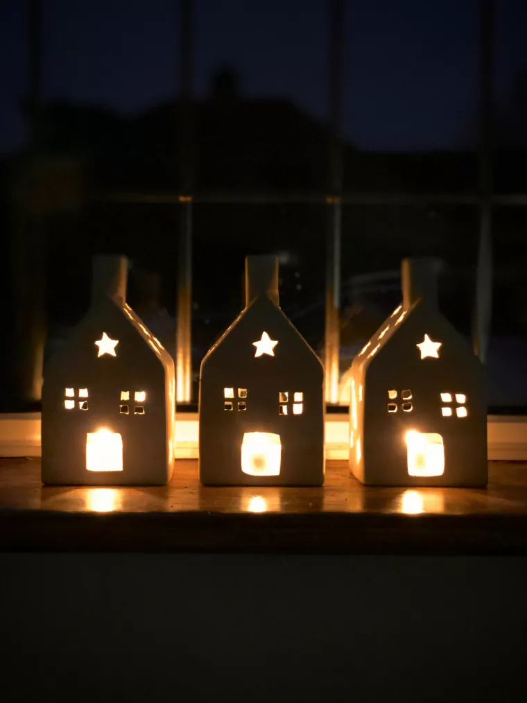 Drei Windlichter in Form von Häusern werden von Kerzen beleuchtet.