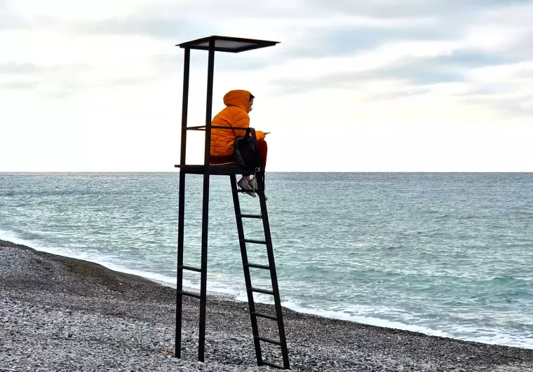 Eine Person sitzt auf einem Badeturm an einem Strand.
