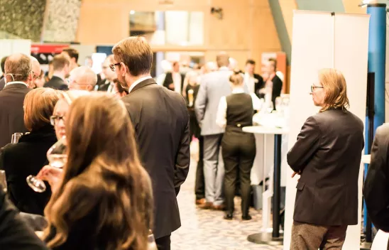 Verschiedene Gruppen stehen in einem Raum an Stehtischen und unterhalten sich