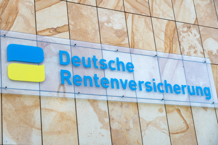 An einer hellen Steinwand hängt ein Glasschild mit der blauen Aufschrift "Deutsche Rentenversicherung". Links neben der Schrift ist ein Zeichen in Form von zwei Sprechblasen in gelb und blau. 