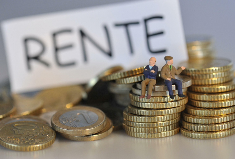 Zwei Rentner als Miniaturfiguren sitzen auf Stapeln von Ein-Euro-Münzen und Fünfzig-Cent-Münzen. Im Hintergrund steht ein Schild mit der Aufschrift "Rente".