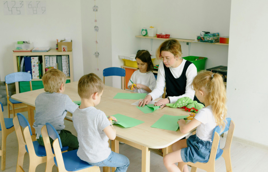 Eine Person sitzt mit mehreren Kindern an einem Tisch und bastelt etwas