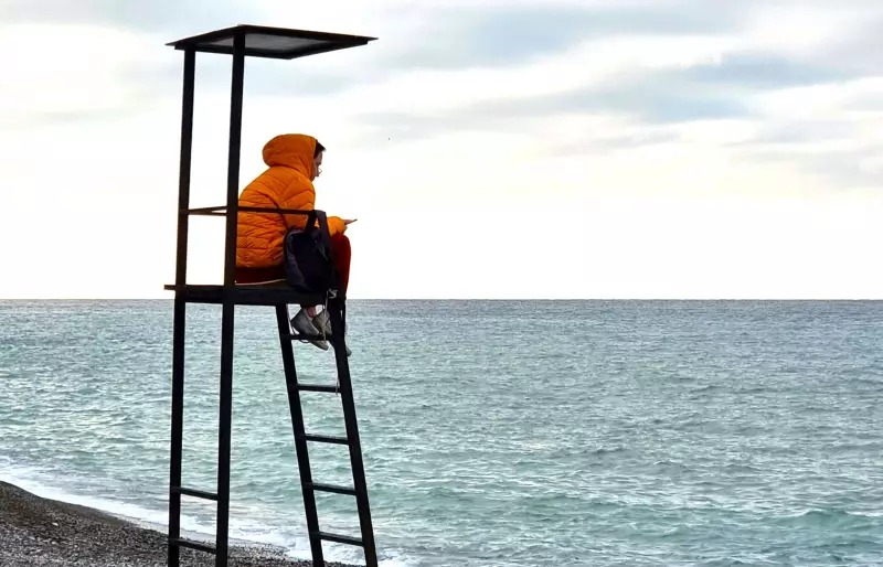 Eine Person sitzt auf einem Badeturm an einem Strand.