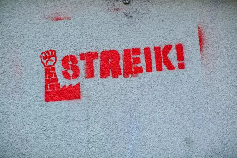 Ein rotes Graffiti an einer hellen Wand zeigt den Schriftzug "Streik!" und eine erhobene Faust.