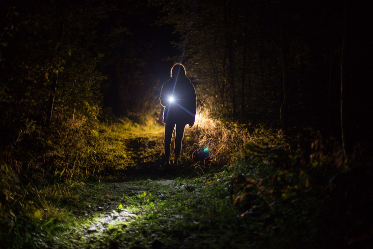 Eine Person steht im Dunkeln und leuchtet mit einer Taschenlampe Richtung Kamera.