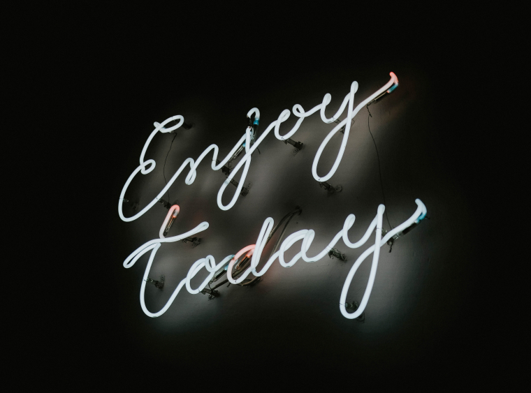 Ein Schriftzug in weißem Neonlicht mit dem Titel "Enjoy today" leuchtet in weiß vor einem dunklen Hintergrund.