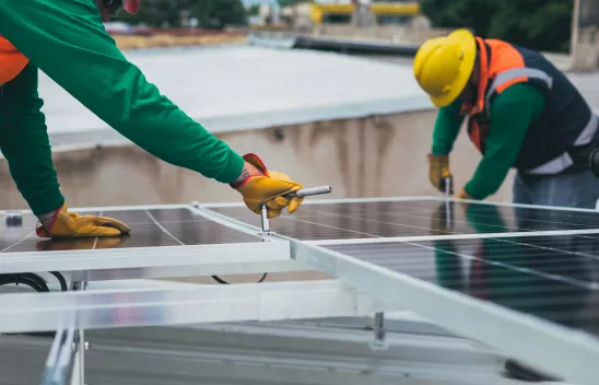 Zwei Personen in Arbeitskleidung arbeiten mit Werkzeug an Solarpanels