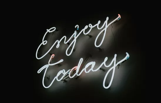 Ein Schriftzug in weißem Neonlicht mit dem Titel "Enjoy today" leuchtet in weiß vor einem dunklen Hintergrund. Ein Schriftzug in weißem Neonlicht mit dem Titel "Enjoy today" leuchtet in weiß vor einem dunklen Hintergrund.