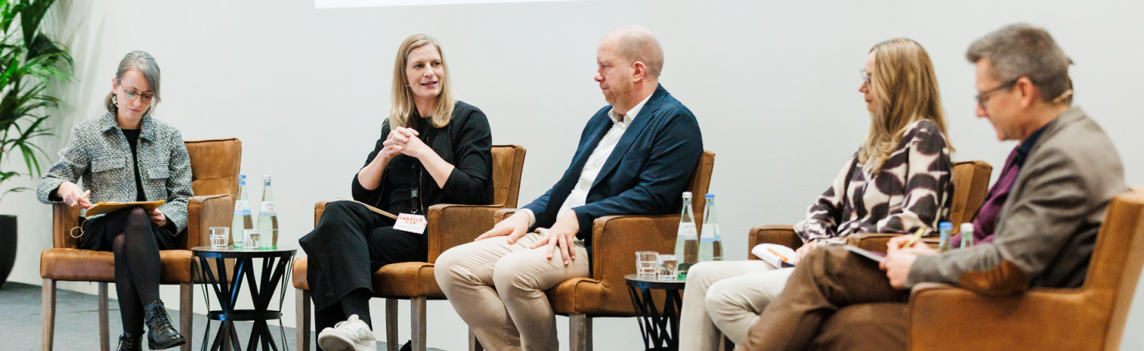 Blick auf eine Bühne, auf der fünf Personen auf dem Podium sitzen